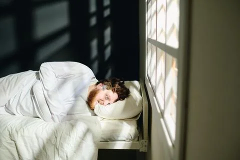 Young deranged man in straitjacket biting pillow while lying on bed Stock Photos