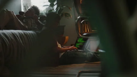 Young Developer Programming on Laptop while His Friend Playing Ukulele Stock Footage 290868445