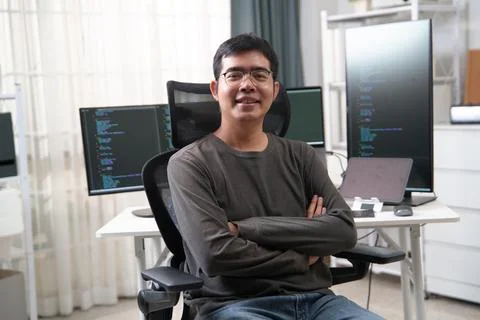 Young Developer Sitting in Front of Dual Monitors Displaying Code for Softwar 库存照片