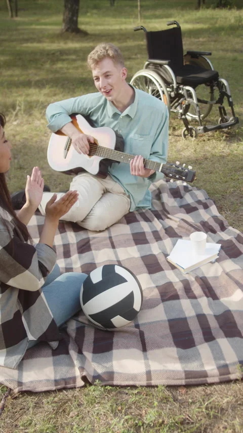 A young disabled man with a guitar in his hand is sitting on the plaid and Stock Footage 173927239