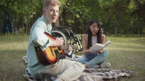 A young disabled man with a guitar in his hand is sitting on the plaid and Stock Footage 174481945