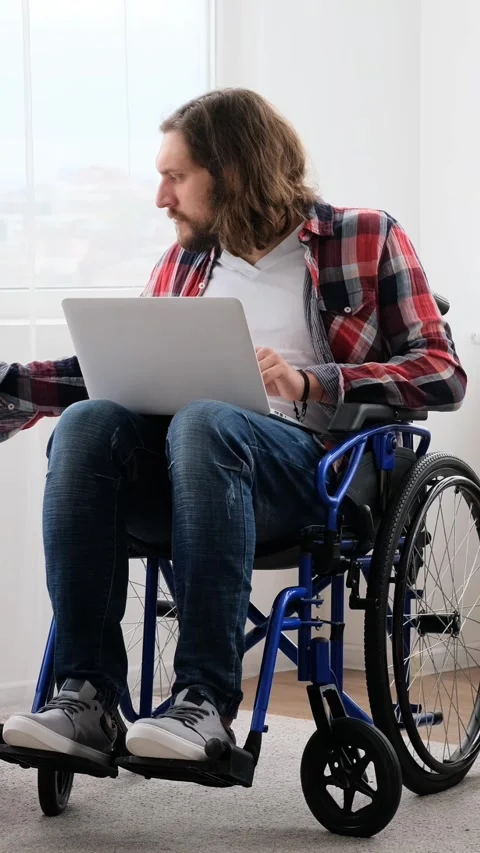 Young disabled man in a wheelchair working remotely on a laptop with documents Stock Footage 328122844