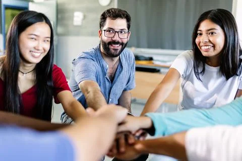 Young diverse group of students stacking hands with male teacher in classroom Stock Photos