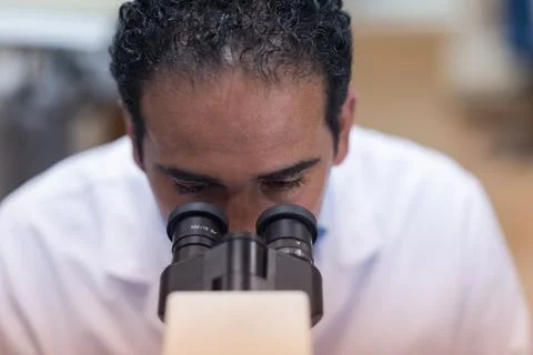 Young doctor examining samples through a microscope in a clinical blood testing 스톡 사진