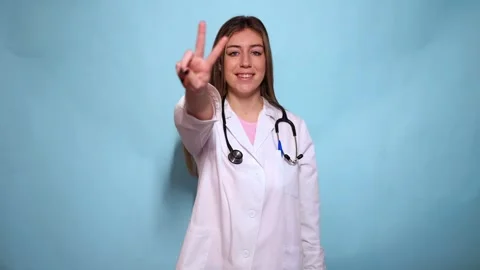 Young doctor gesturing and counting with fingers on blue background Stock Footage 297675211