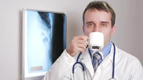 A young doctor looking at the camera is drinking a hot drink from a white mug Stock Footage 73962459