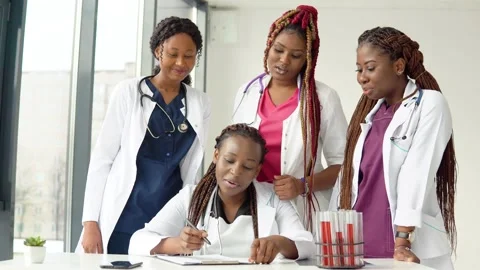 Young doctors have a discussion standing at a table while one of them makes Stock Footage 148236276