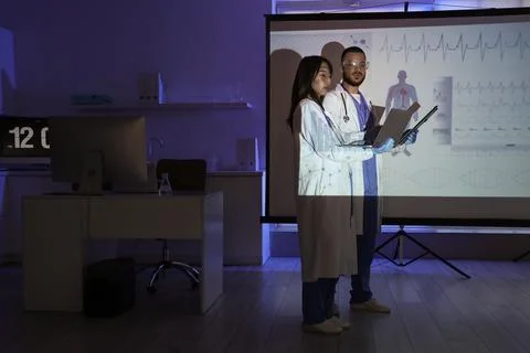 Young doctors with laptop analyzing scientific data near projector screen in  Stock Photos