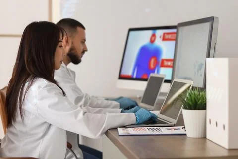 Young doctors with laptops analyzing scientific data at desk in laboratory Stock Photos