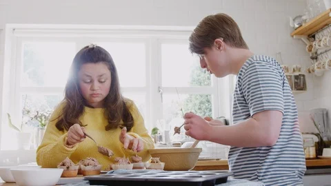 Young Downs Syndrome Couple Decorating Homemade Cupcakes With Icing In Kitchen Stock Footage 114303962
