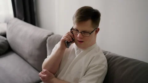 Young Downs Syndrome guy sitting on sofa using mobile phone at home Stock Footage 242223487