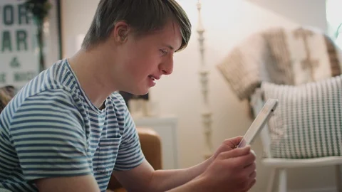 Young Downs Syndrome Man Sitting On Sofa Watching Digital Tablet At Home Stock Footage 114305022