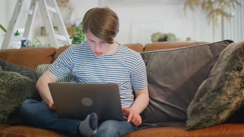 Young Downs Syndrome Man Sitting On Sofa Using Laptop At Home Stock Footage 114305409