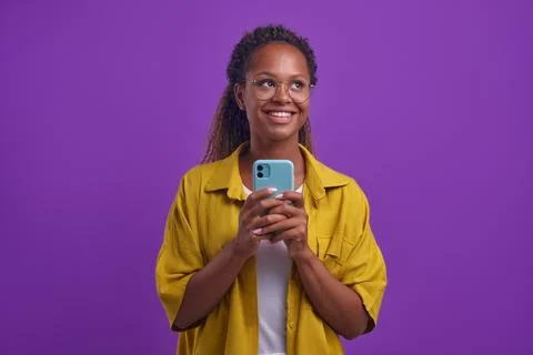 Young dreamy African American woman holds phone flirting in online chat Stock Photos