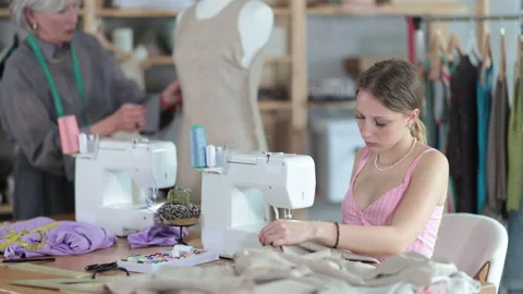 Young dressmaker works on a sewing machine against the background of a mature Stock Footage 341382035