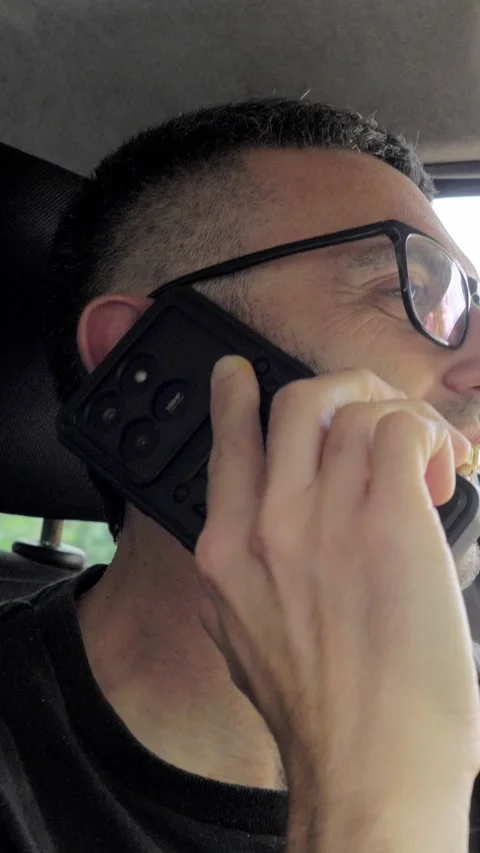 Young Driver Smiling on Phone Call Behind the Wheel, Unaware of Road Risk Stock Footage 335701701