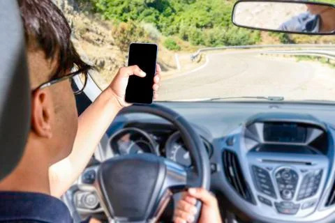 Young driver, using smartphone, on the road in the car. Stock Photos