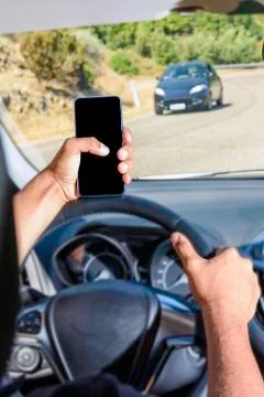 Young driver, using smartphone, on the road in the car. Stock Photos