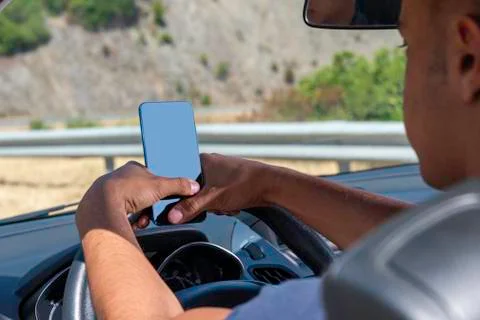 Young driver, using smartphone, on the road in the car. Stock Photos
