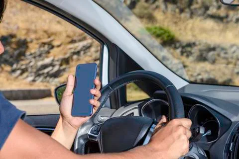 Young driver, using smartphone, on the road in the car. Stock Photos