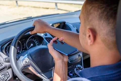 Young driver, using smartphone, on the road in the car. Stock Photos