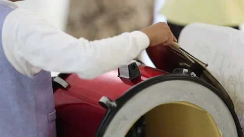 Young drummer striking cymbal on red bass drum in indoor rehearsal with soft Stock Footage 346083406
