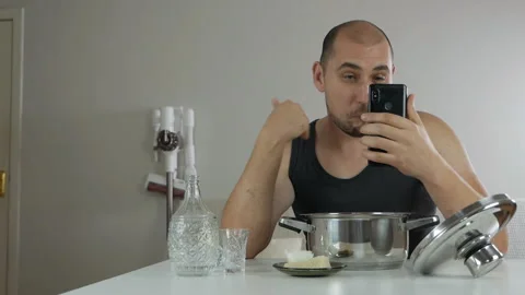 A young drunk guy at home alone at the table drinks alcohol, communicating by Stock-Footage 143117307