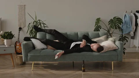 Young drunk guy sleeping on the couch in a suit wakes up in the morning with a Stock Footage 167807084