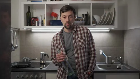 Young drunk man alone in kitchen at night, holding an empty wine bottle. Talks Stock Footage 330902762