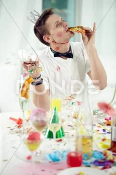 Young drunken man eating and drinking up remnants of festive meal after party Stock Photos