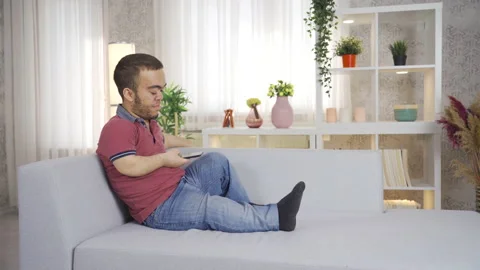 Young dwarf man sitting on sofa at home and using smartphone. 動画素材 230965822