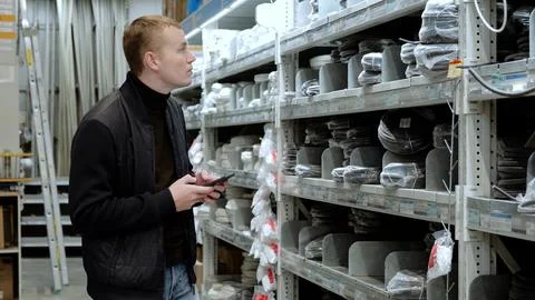 Young electrician browsing electrical cables on smartphone in hardware store 写真素材