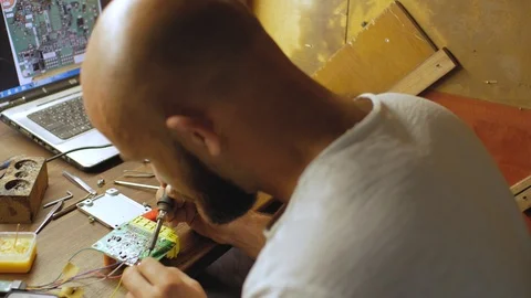 Young electronics engineer with a beard solders an electrical board.4 k video Stock Footage 108185329