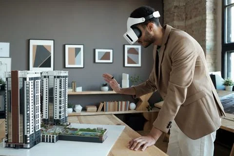 Young elegant architect standing by table with house layout during presentation Stock Photos