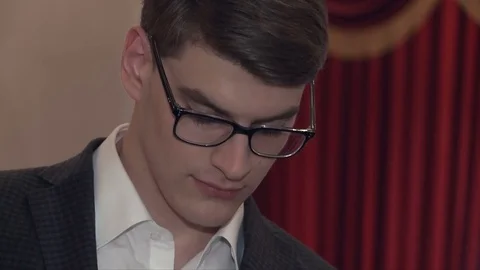 A young elegant man in glasses and a suit is standing in the theater and enjoys Video stock 77201826