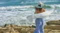 Young elegant woman holding scarf in wind, ocean waves crashing on rocky beach HD Footage