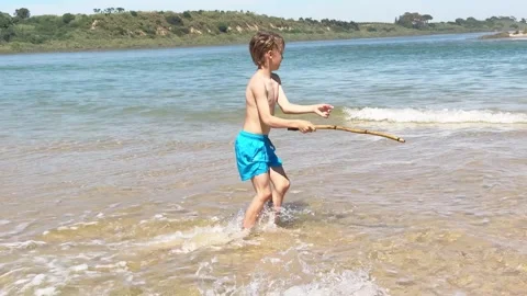 Young energetic boy happily jumping and running in the shallow water of a sunny Vidéo 333283094