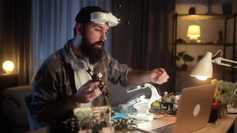 A young engineer with a beard is assembling, soldering, programming, and testing Video stock 256635177