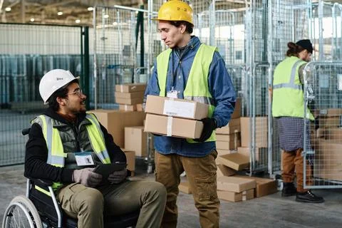 Young engineer with boxes talking to colleague in wheelchair using tablet Stock Photos