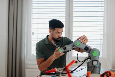Young engineer building and programming a robotic arm at home. Stock Photos