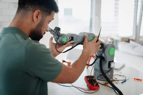 Young engineer building and programming a robotic arm at home. Stock Photos