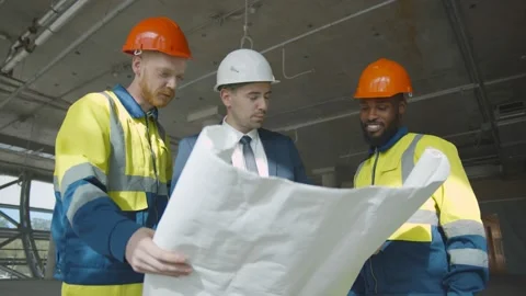 Young engineer discussing blueprint with building workers on construction site Stock Footage 137327979