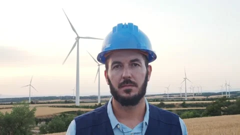 Young engineer man ooking seriously at camera in a field of windmills. Stock Footage 198423029