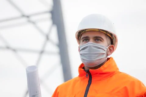 Young engineer or architect with face mask and plan in his hand wearing prote Stock Photos