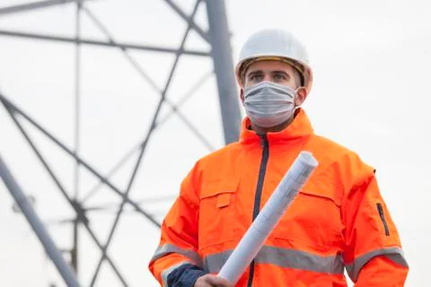 Young engineer or architect with face mask and plan in his hand on constructi Stock Photos