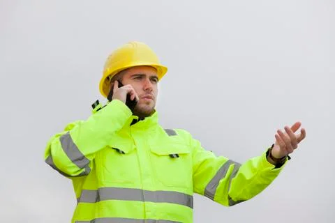 Young engineer or worker with green protective work wear talking on mobile ph Stock Photos
