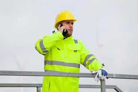 Young engineer or worker talking on smart phone in front of wind turbines Фото