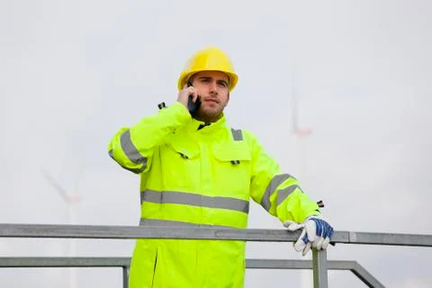 Young engineer or worker talking on smart phone in front of wind turbines Stock Photos