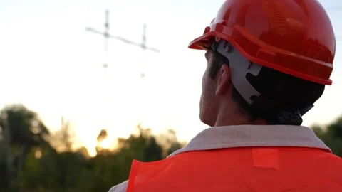 Young engineer standing outdoors while looking at the high voltage power lines Stock Footage 255391202