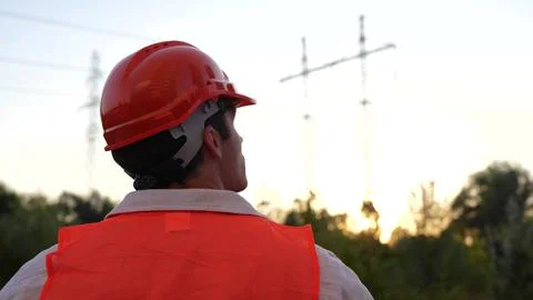Young engineer standing outdoors while looking at the high voltage power lines Stock Photos